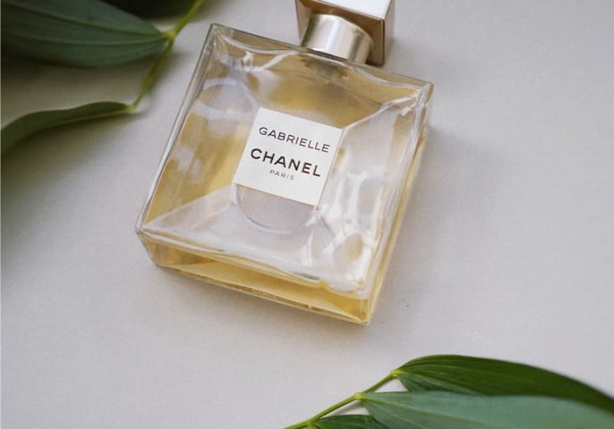 A Channel bottle of perfume is on a table surrounded by green leaves.